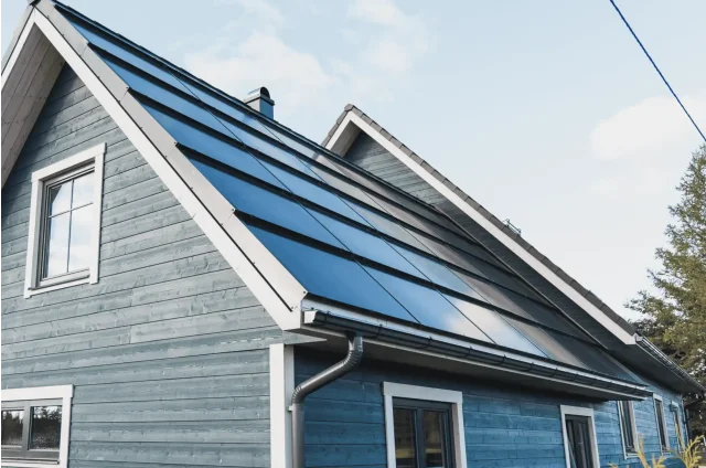Blue wooden house with integrated solar panels covering the pitched roof.