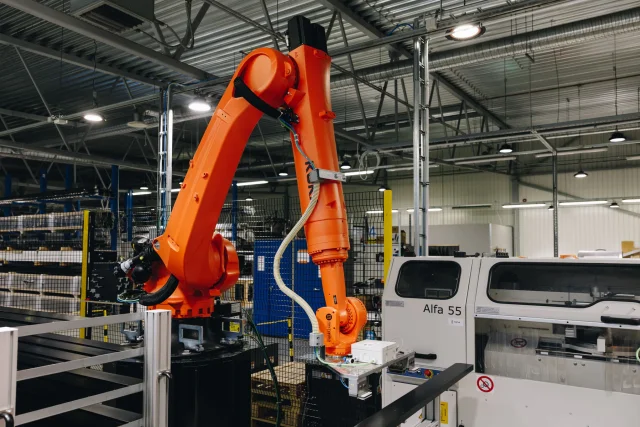 Industrial robot positioned beside an aluminium profile processing machine.