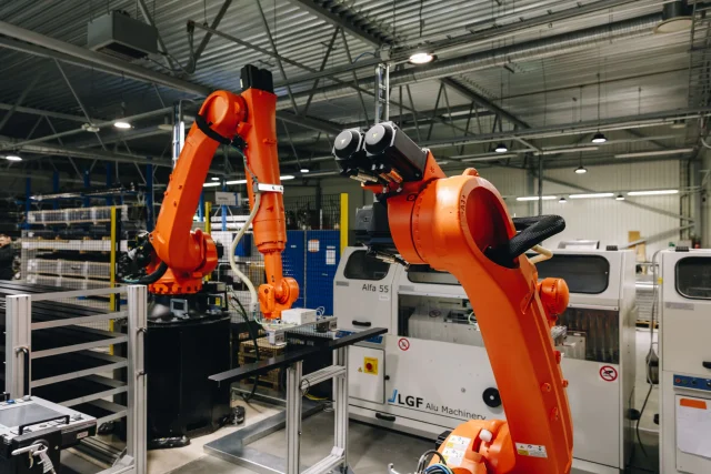 Industrial robots working beside aluminium profile processing machinery.