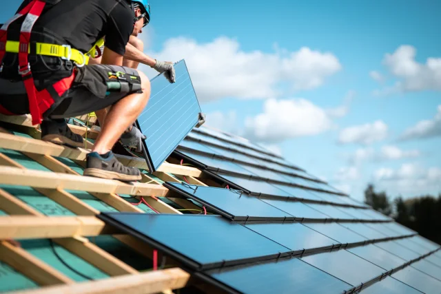 Two installers lowering a Solar Tiled Roof™ module into place on timber battens.