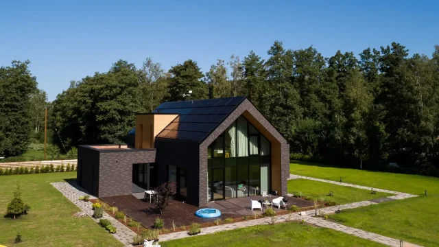 Aerial view of a modern dark-brick home with an integrated solar roof.