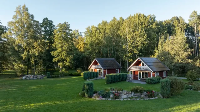 Aerial view of two red cottages with integrated solar roofs beside a landscaped garden.
