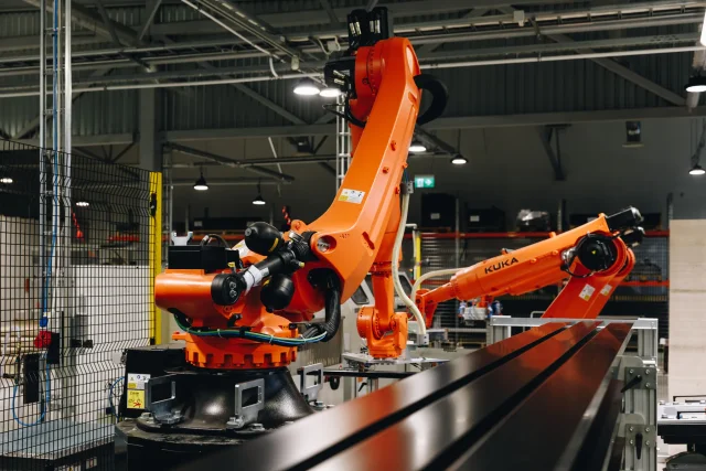 Industrial robot arms handling black metal profiles inside the Solarstone factory.