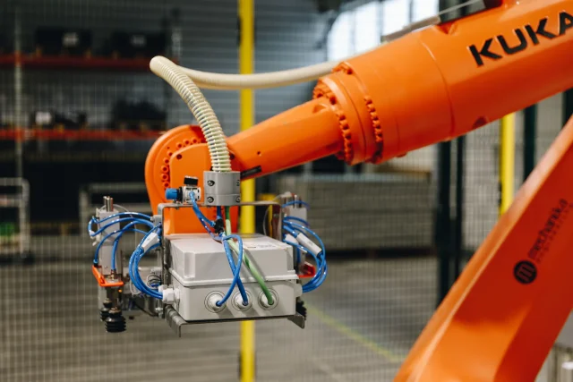 Close-up of an industrial robot gripper with pneumatic lines and control components.