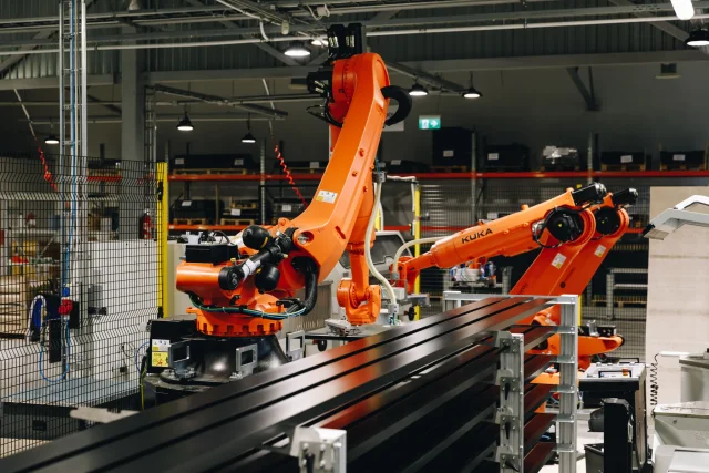 Industrial robots positioned beside black metal profiles on the automated production line.