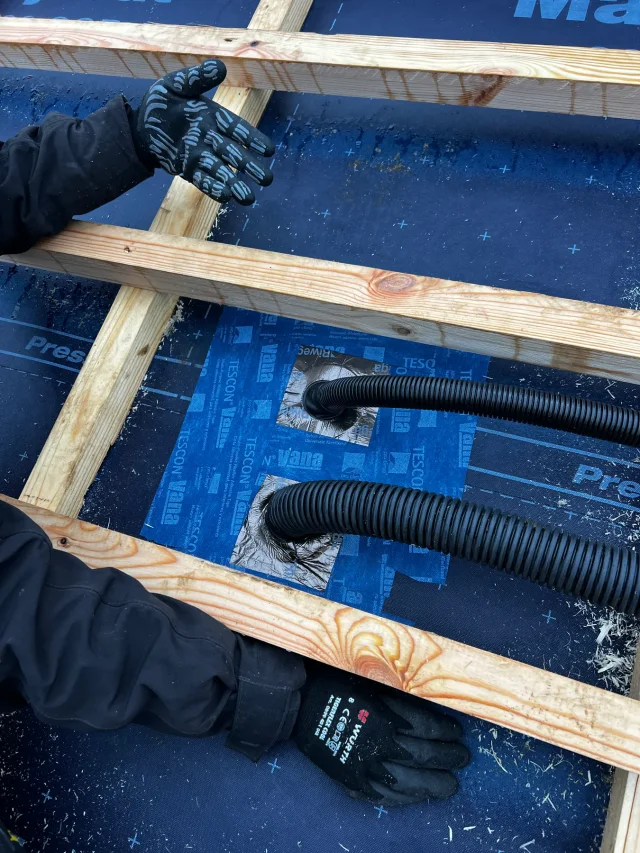 Installers routing corrugated electrical cables between roof battens for a Solar Full Roof™ system.