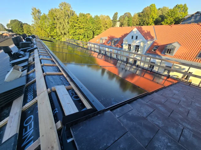 View along aligned Solar Full Roof™ module rows beside a riverside roof.