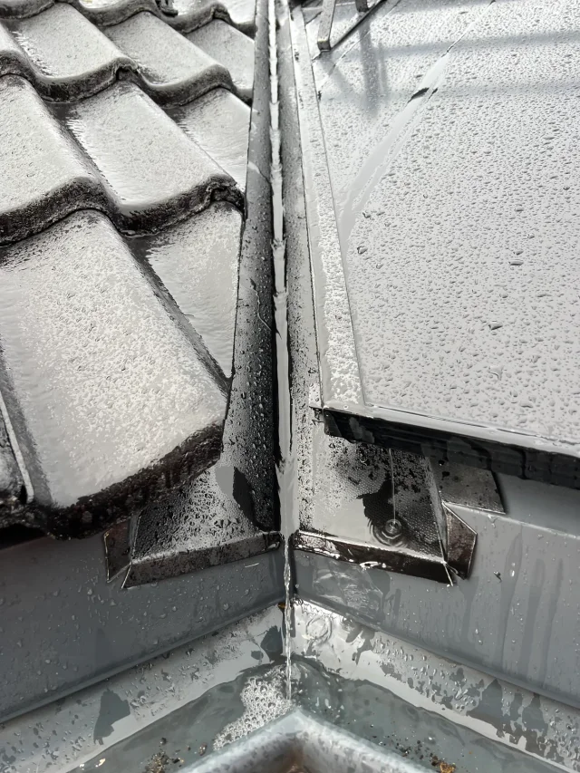 Close-up of metal valley flashing between grey roof tiles and a Solar Full Roof™ installation.