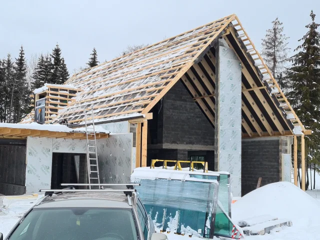 Timber roof framing for a Solar Full Roof™ project at a snow-covered construction site.