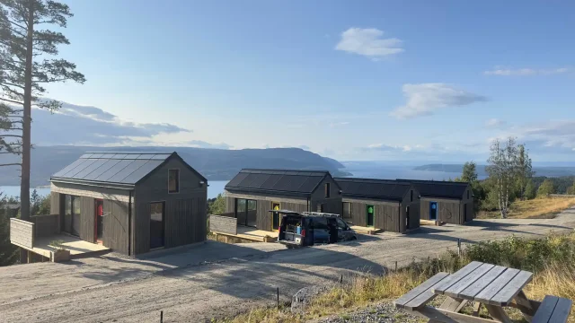 Timber cabins with integrated solar roofs overlooking a Norwegian fjord.