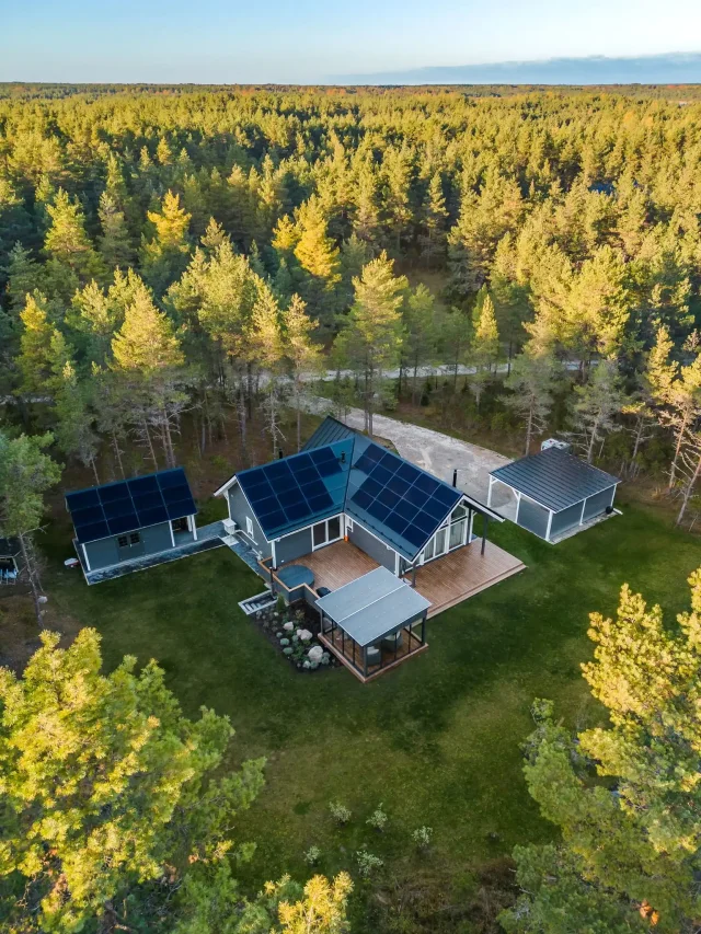 Aerial view of a home with an integrated solar roof surrounded by forest.