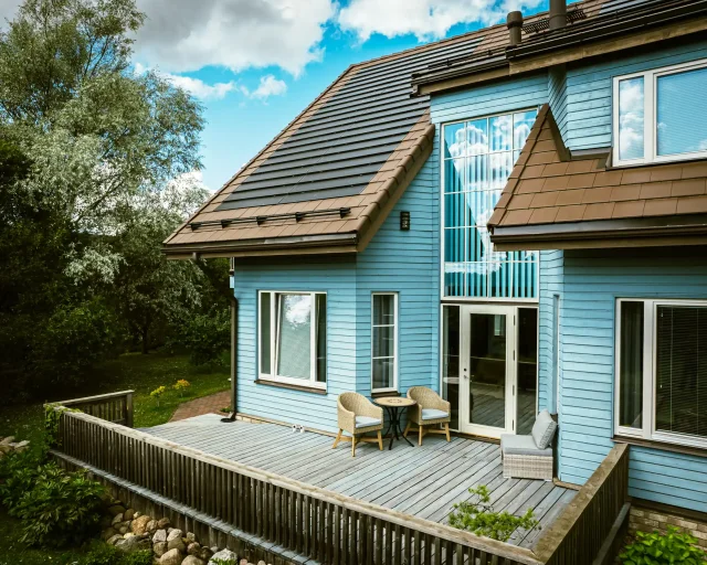 Blue wooden home with a Solar Tiled Roof™ installation and garden terrace.