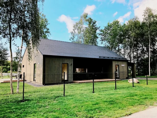 Modern dark timber building with a Solar Tiled Roof™ installation in a green, wooded setting.