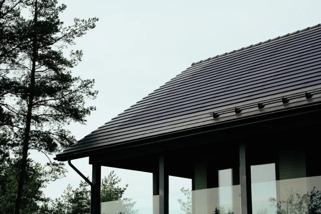 Low-angle view of a Solar Tiled Roof™ installation on a dark timber home framed by pine trees.