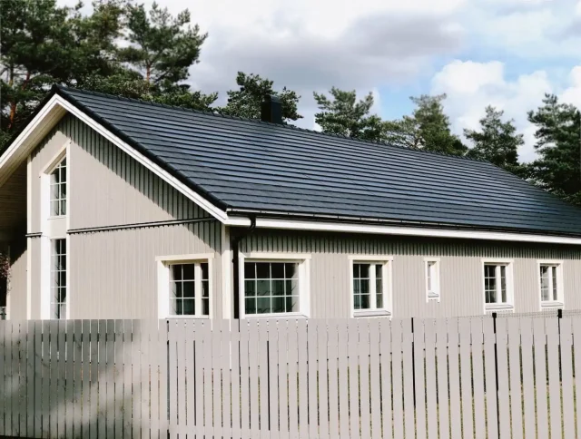 Light-grey wooden home with a dark Solar Tiled Roof™ installation and a white picket fence.
