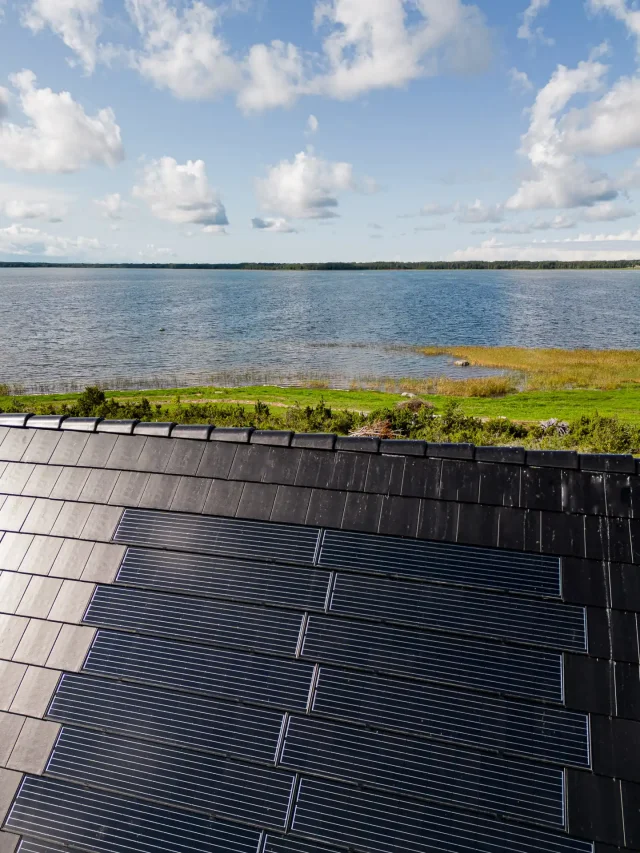 Solar Tiled Roof™ installation on a lakeside home overlooking the water beneath a blue, cloudy sky.