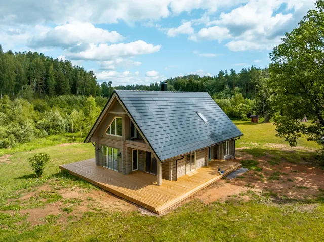 Aerial view of a log home with a Solar Tiled Roof™ installation in a forest clearing.