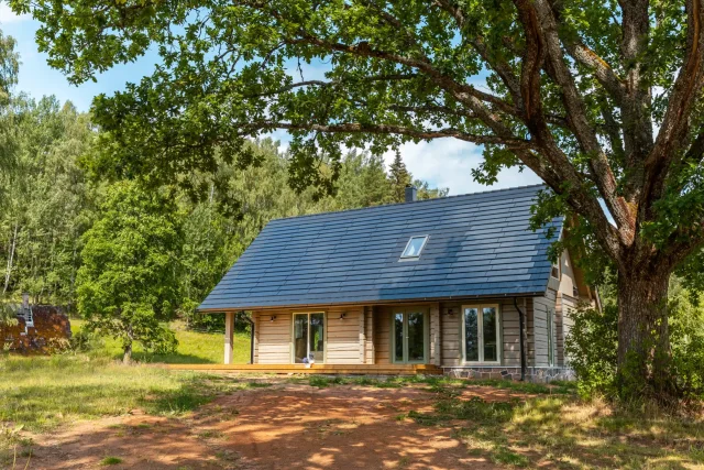 Log home with a Solar Tiled Roof™ installation framed by a large oak tree.
