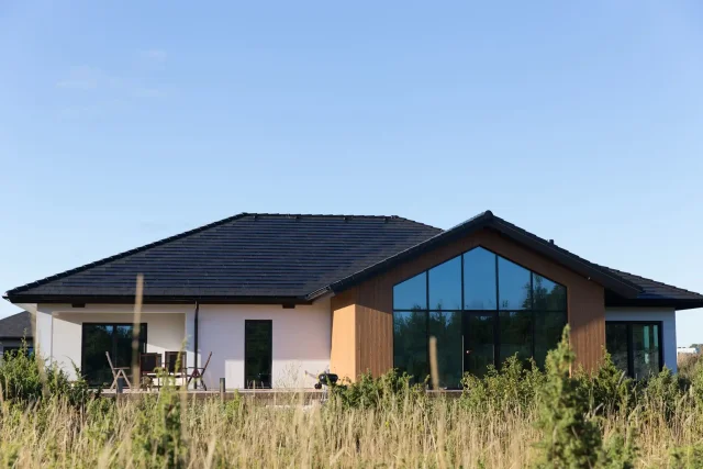 Modern single-story home with a Solar Tiled Roof™ installation, timber cladding and a large glass façade.