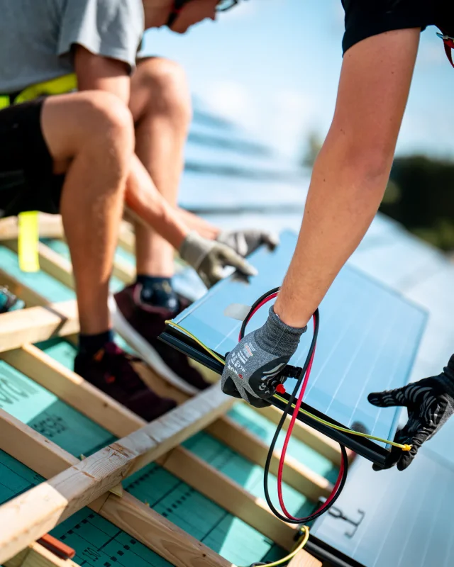 Installers positioning a Solar Tiled Roof™ module with its electrical cables over timber battens.