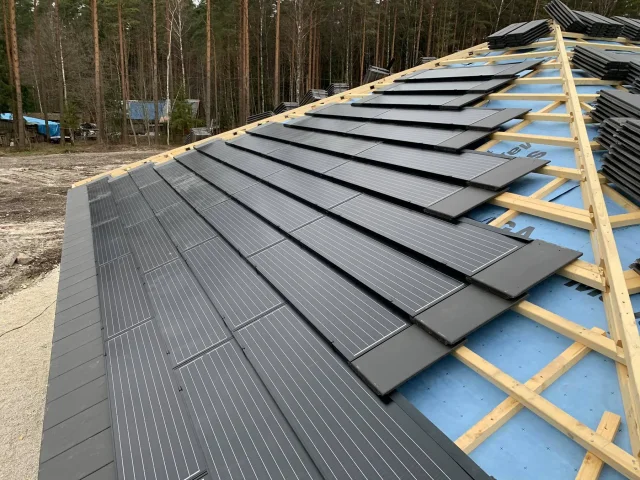Rows of Solar Tiled Roof™ modules being installed on timber battens beside a forest.