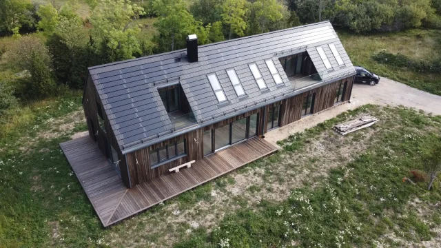 Aerial view of a long timber-clad home with a Solar Tiled Roof™ installation, skylights and recessed roof terraces.