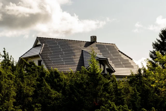 Solar Tiled Roof™ installation on a traditional home with a chimney, partly surrounded by trees.