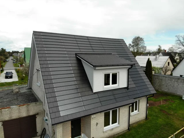 Aerial view of a white brick house with a dark Solar Tiled Roof™ installation and dormer window.