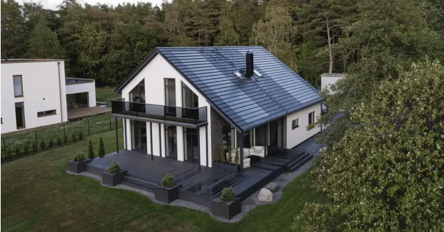 Aerial view of a white modern home with a Solar Tiled Roof™ installation, balcony and dark wooden terrace.