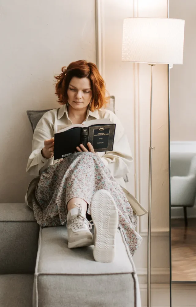 Woman reading a book on a sofa beside a floor lamp at home