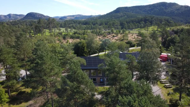 Aerial view of a woodland home with an integrated solar roof and mountain landscape.