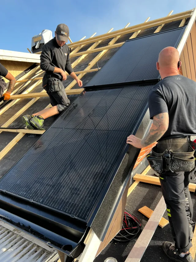 Two installers positioning a Solar Full Roof™ module on timber roof battens.